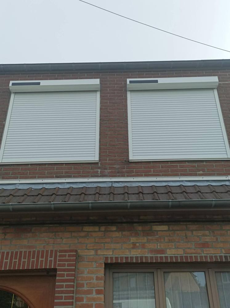 Deux volets roulants motorisés blancs installés en façade, maison en briques